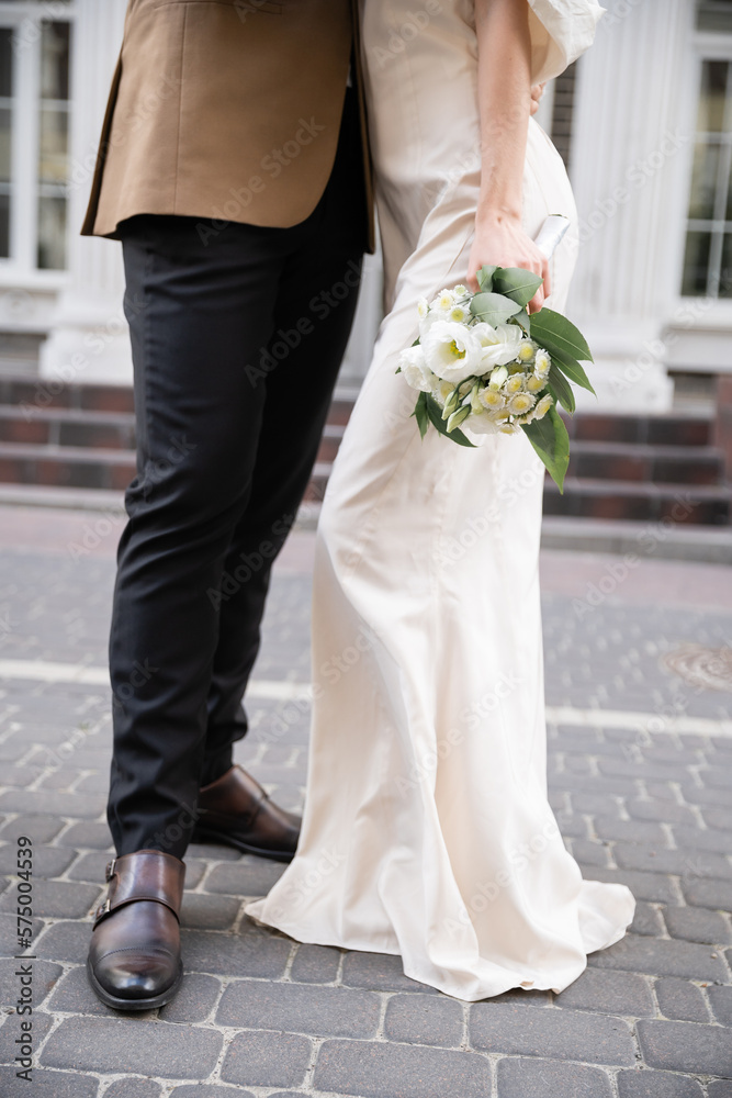 cropped view of groom in suit standing with bride in white dress holding wedding bouquet. cropped view of groom in suit standing with bride in white dress holding wedding bouquet.