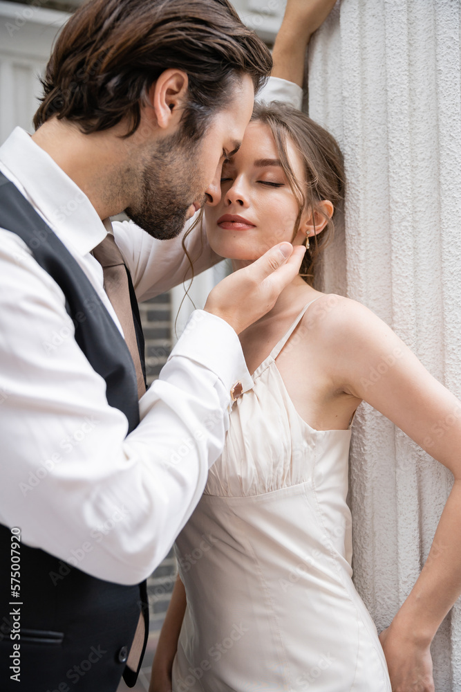 bearded groom in formal wear touching face of pretty bride with closed eyes. bearded groom in formal wear touching face of pretty bride with closed eyes.