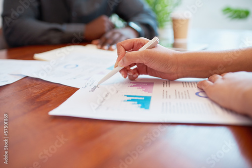 Close up of woman's hands holding pen pointing to financial report in meeting