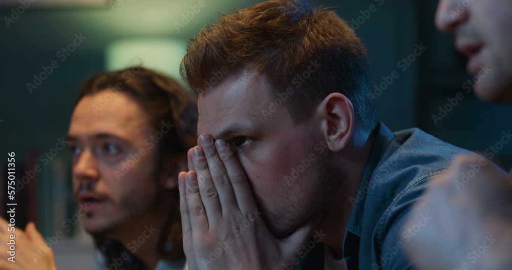 Close up of handsome Caucasian men football fans sitting on couch and watching football match late at night. Guys cheering and worrying for favorite team which missing goal and loosing in game.