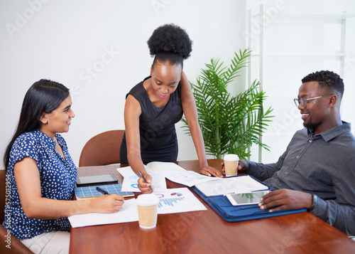 Three business colleagues discuss financial reports around boardroom table