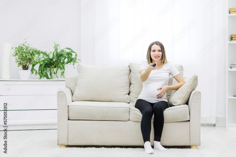 Photo of pregnant young woman with remote control in hand. Photo of pregnant young woman with remote control in hand.
