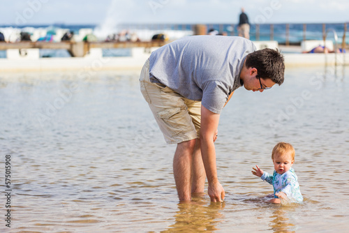 Happy young baby girl sitting in shallow sea water in ocean pool at beach in summer photo