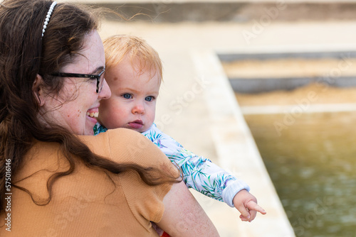 Mother holding little girl walking away from ocean baths with baby pointing at water photo