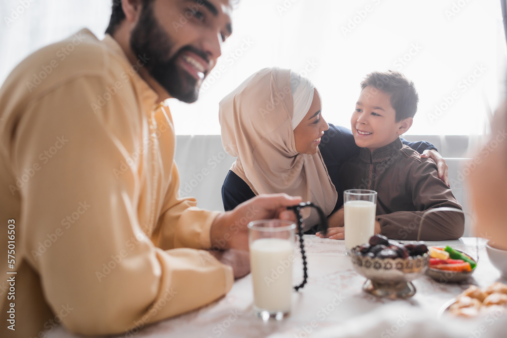 Positive african american mother in hijab hugging son near family and suhur breakfast at home. Positive african american mother in hijab hugging son near family and suhur breakfast at home.