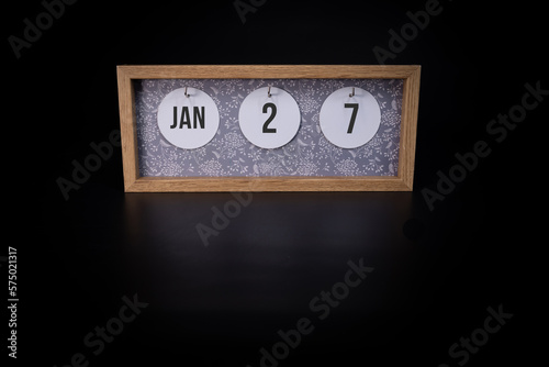 A wooden calendar block showing the date January 27th on a dark black background, save the date or date of event concept