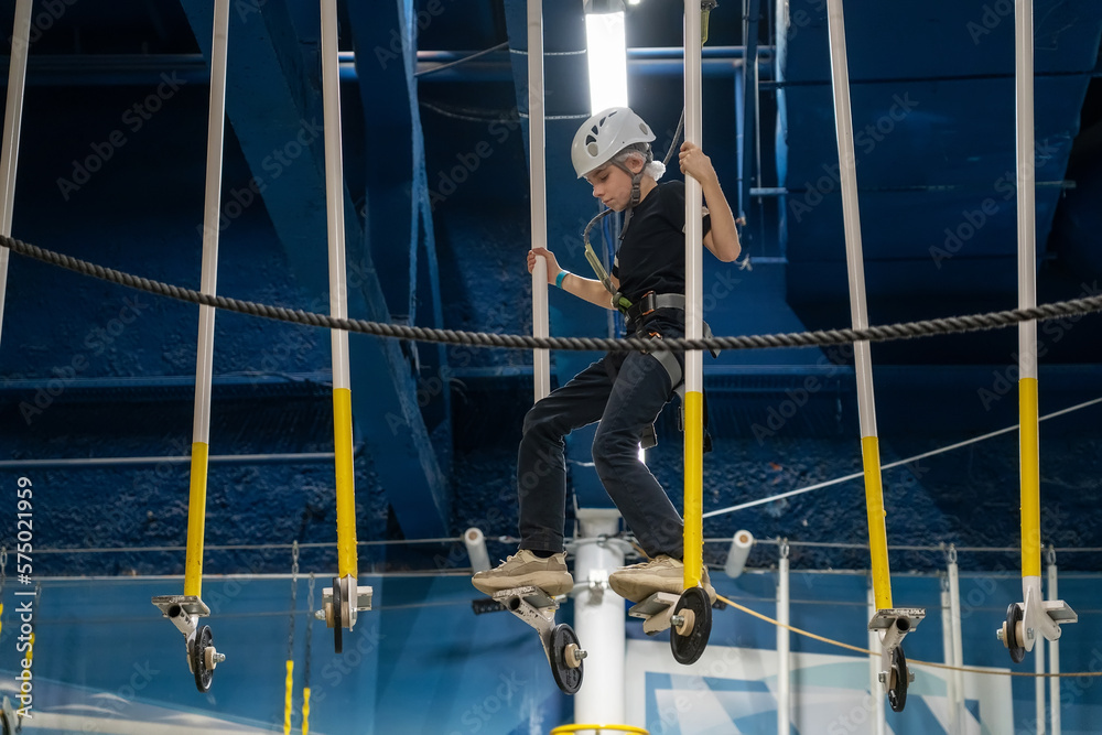 Teenage boy in white helmet calmly overcomes balancing obstacles in rope park