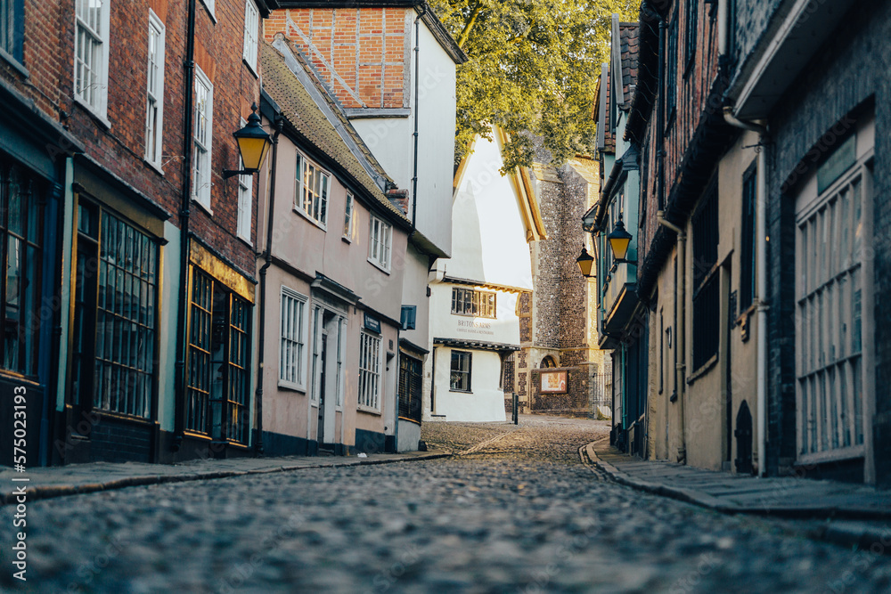 Low down photo of an old English cobbled road and a row of shops, traditional historic buildings, beautiful town