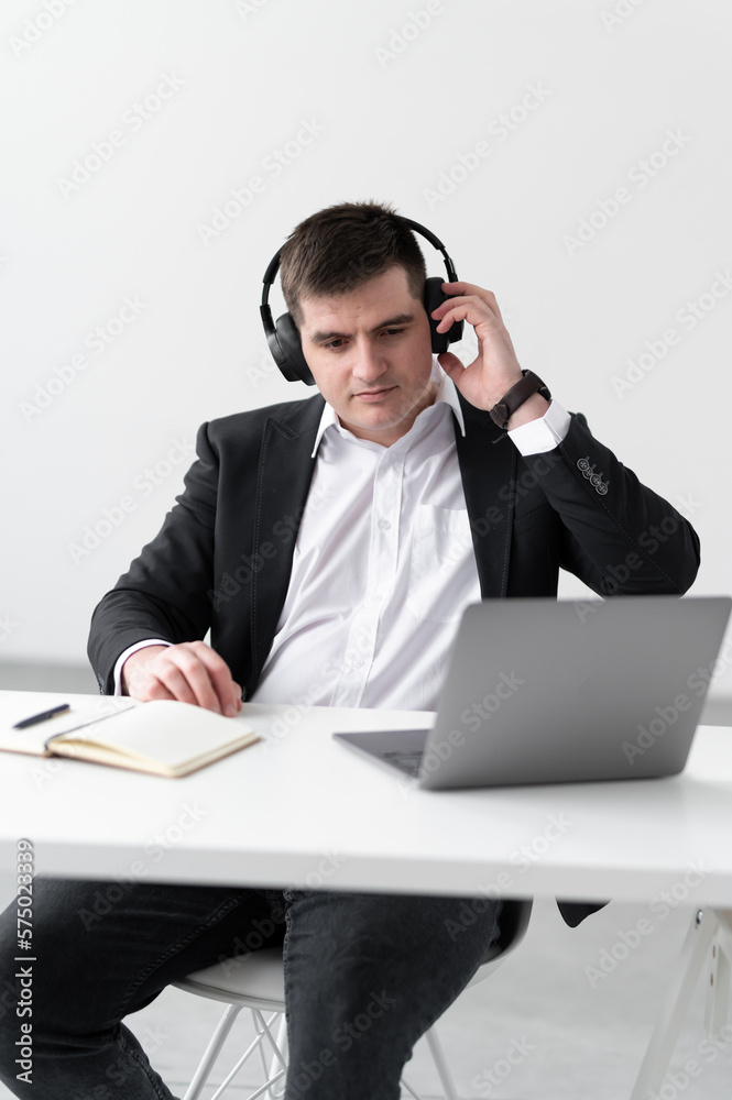 Focused young european man wear headphones, studying online, watching webinar podcast on laptop, listening to study, education course, conference calling, taking notes, sitting at desk Focused young european man wear headphones, studying online, watching webinar podcast on laptop, listening to study, education course, conference calling, taking notes, sitting at desk