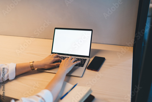 Unrecognizable woman sitting at desk and working on laptop in office