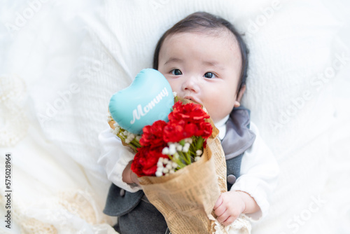 母の日にカーネーションの花束をプレゼントしようとママを見つめる赤ちゃん photo