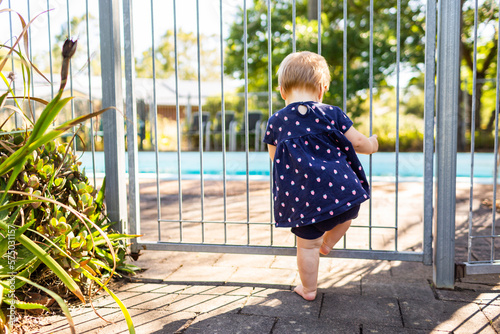 Young child standing at self closing pool gate safe behind fence photo