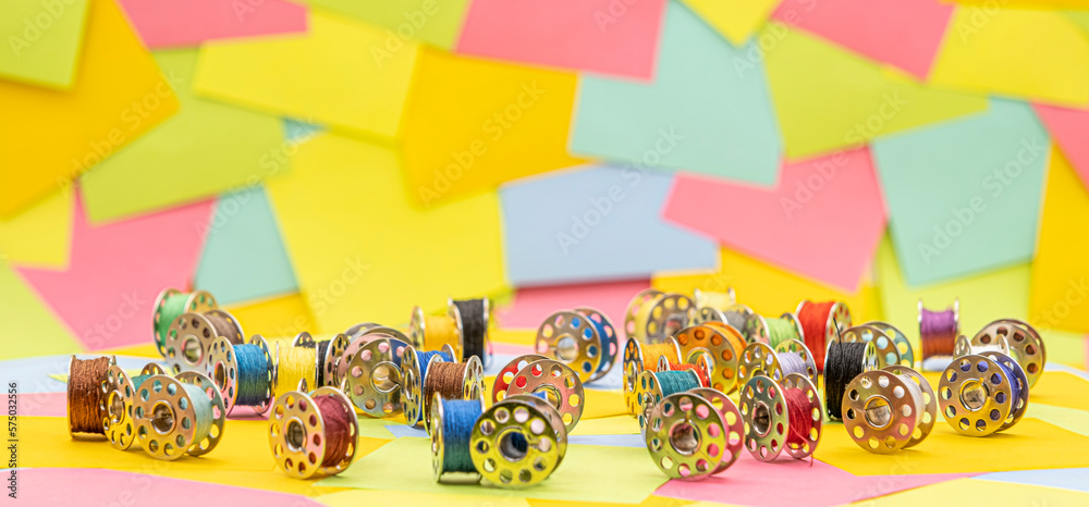 metal spools with Multicolored thread for sewing machine on a  table with multicolored paper sticky notes on background