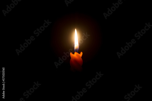 A single burning candle flame or light glowing on a beautiful spiral orange candle on black or dark background with copy space for text on table in church for Christmas, funeral or memorial service.