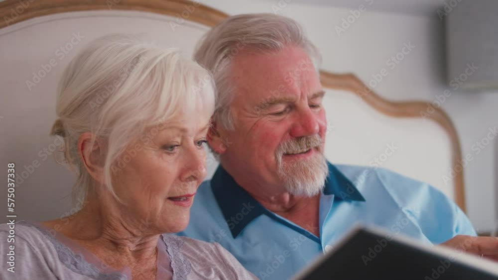 Close up of smiling retired senior couple in bed at home looking through photo album and reliving old memories - shot in slow motion Close up of smiling retired senior couple in bed at home looking through photo album and reliving old memories - shot in slow motion