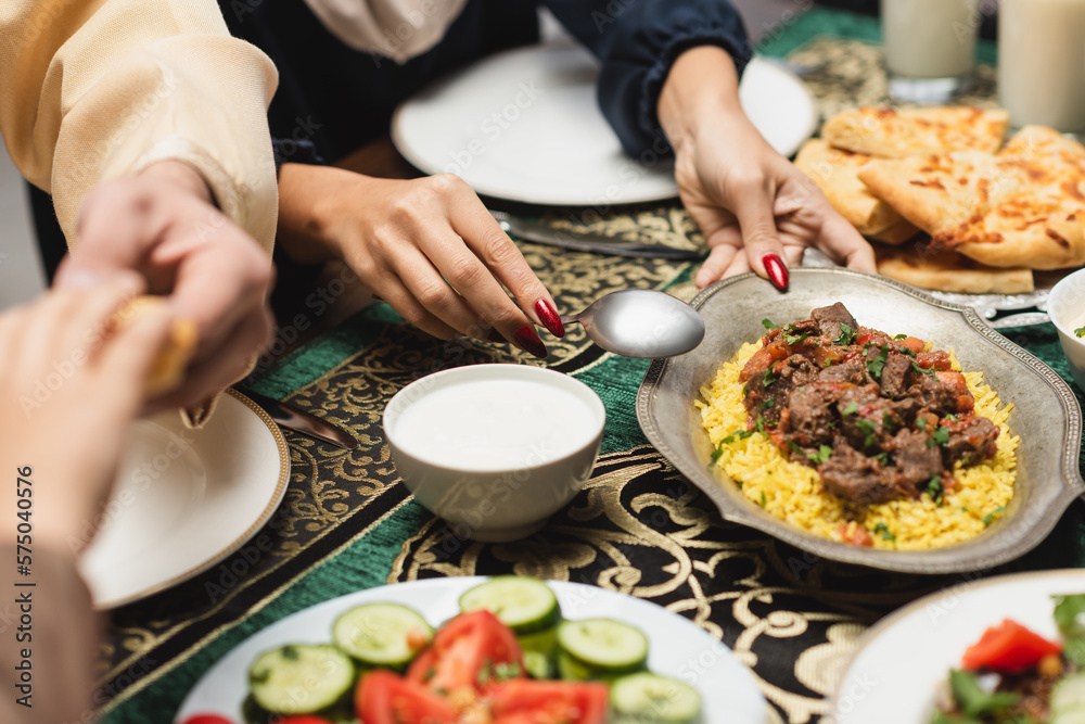 Cropped view of muslim woman putting pilaf on table during ramadan dinner.