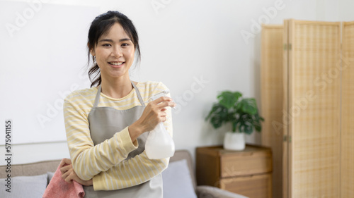 Asian housewife wearing apron holding rag and cleaning spray prepares for a big cleanup in the house, Housework, Daily routine, Big cleaning, Deep stain remover, Clean up on weekends.