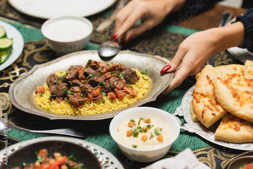 Cropped view of muslim woman putting pilaf on table during iftar at home.