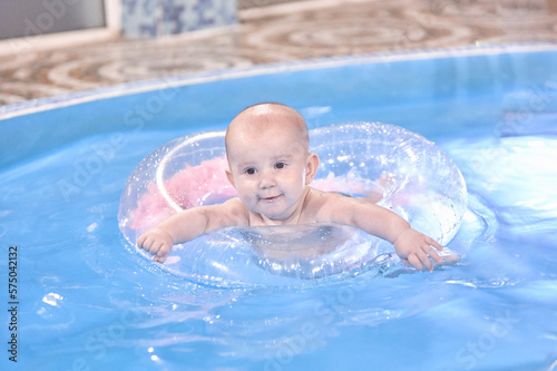 A small child aged 6 months swims in the pool  swims on a balloon  mom helps him stay in the balloon.