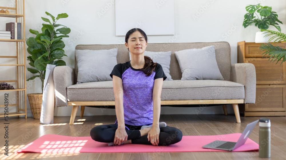 Beautiful healthy woman practicing yoga, Stretch or warm up before exercising, Calming the mind and meditating in her living room, Dumbbells and a protein shake or bottle of water, Healthy exercise. Beautiful healthy woman practicing yoga, Stretch or warm up before exercising, Calming the mind and meditating in her living room, Dumbbells and a protein shake or bottle of water, Healthy exercise.