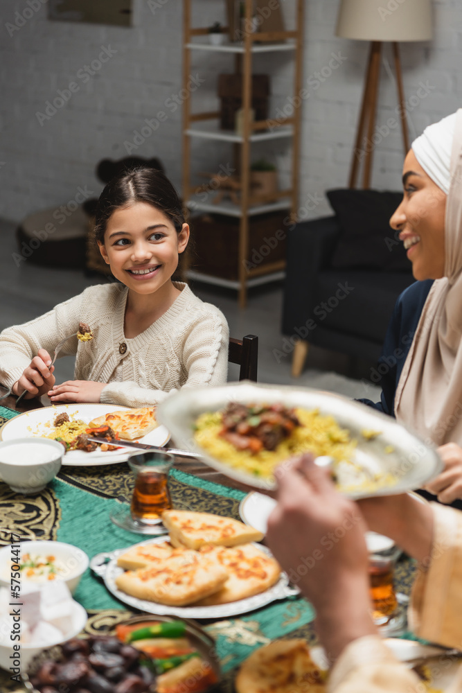 Smiling muslim girl looking at parents near food during ramadan at home.