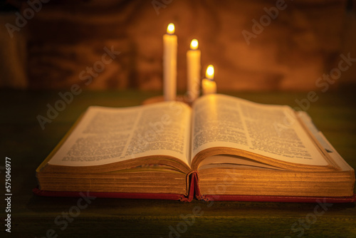 closeup of a bible with three candles out of focus in the background