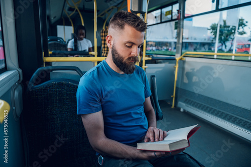 Man reading a book while riding in a bus
