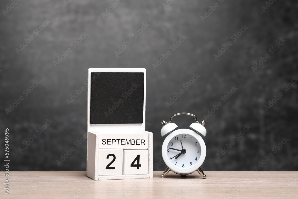 Wooden Calendar with september 24 date and alarm clock on table against chalk board background Wooden Calendar with september 24 date and alarm clock on table against chalk board background