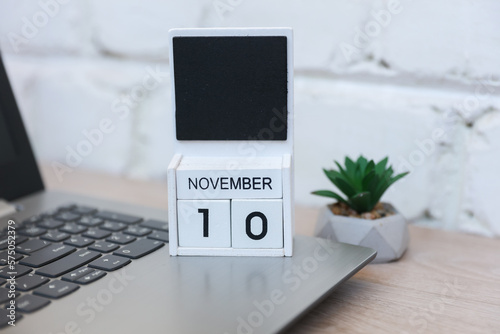 Wooden calendar with date November 10 and laptop on table against brick wall background. Deadline, planning, business concept