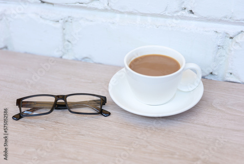 Eyeglasses and coffee cup on table against a brick wall. Coffee break photo