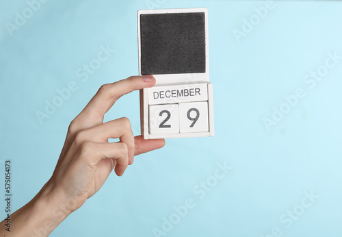 Female hand holding wooden calendar with date december 29 isolated on blue background