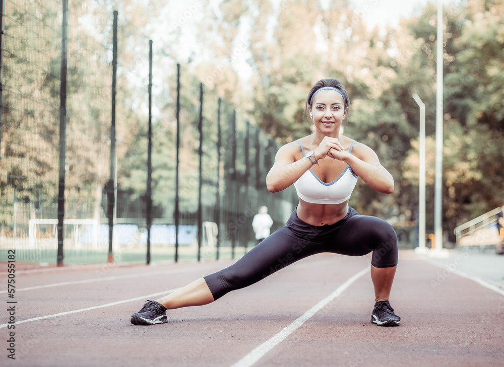 Beautiful muscular woman practicing side lunges in the stadium. Leg workout. Healthy lifestyle Beautiful muscular woman practicing side lunges in the stadium. Leg workout. Healthy lifestyle