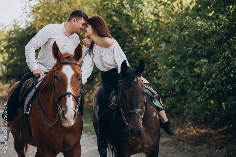 Fototapeta premium Young couple riding horses together in park