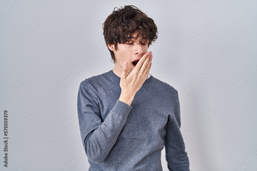 Young man standing over isolated background bored yawning tired covering mouth with hand. restless and sleepiness. Young man standing over isolated background bored yawning tired covering mouth with hand. restless and sleepiness.