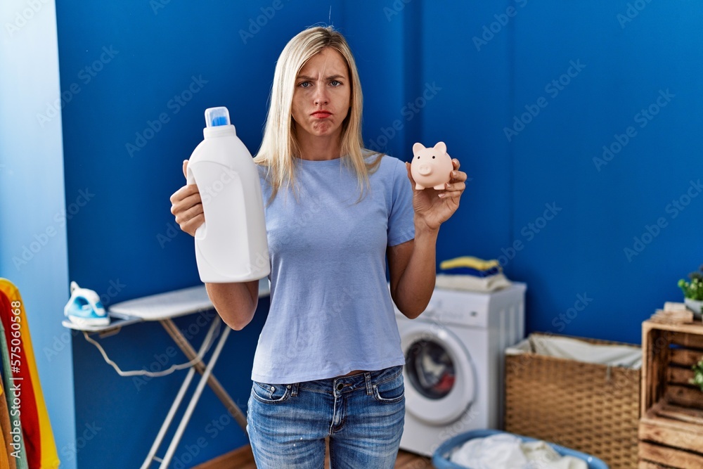 Φωτογραφία Beautiful woman doing laundry holding detergent bottle and piggy bank skeptic and nervous, frowning upset because of problem