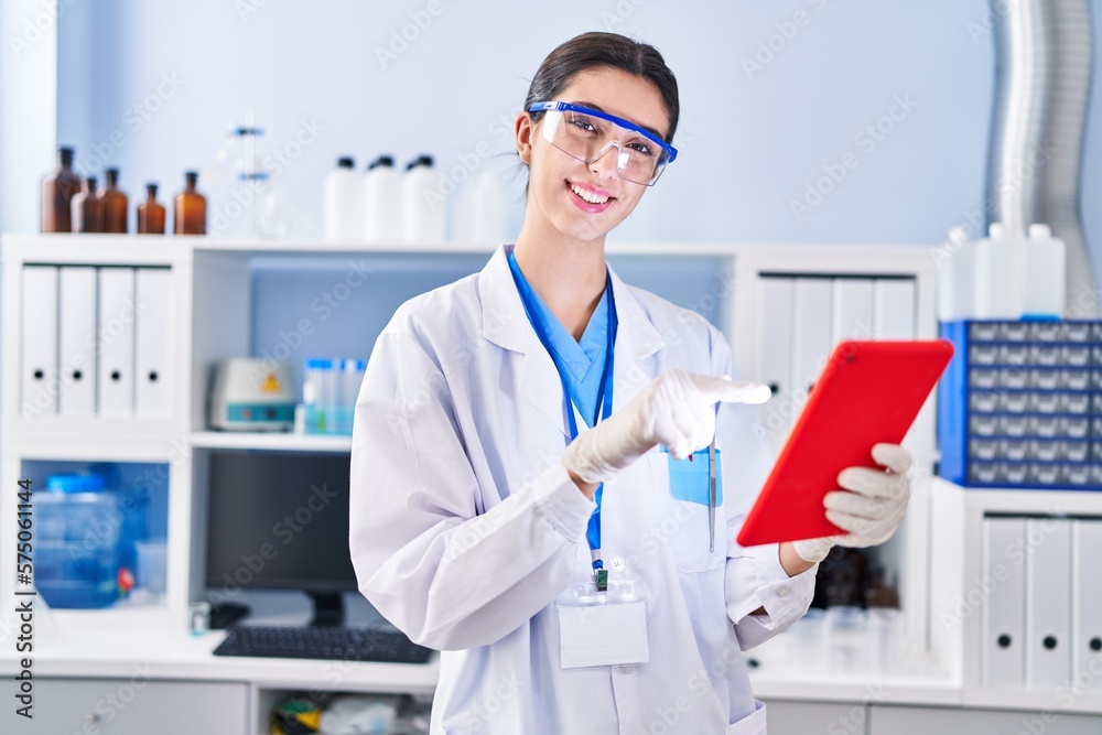 Young beautiful hispanic woman scientist smiling confident using touchpad at laboratory