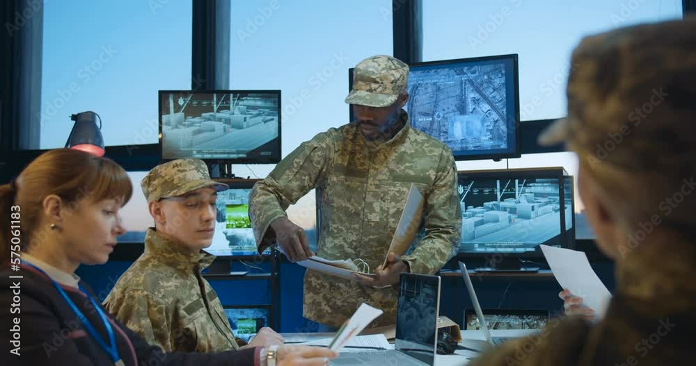 African American young military male general handing documents to Caucasian army staff at meeting. Conference on army studing and planning. Brainstorming of naval strategy. Troops studying.