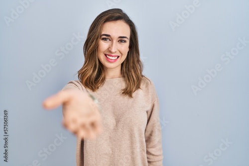 Young woman standing over isolated background smiling cheerful offering palm hand giving assistance and acceptance.