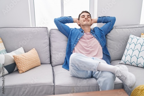 Young hispanic man relaxed with hands on head sitting on sofa at home