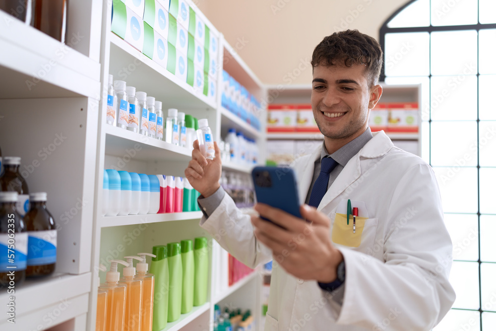 Young hispanic man pharmacist using smartphone holding medication bottle at pharmacy