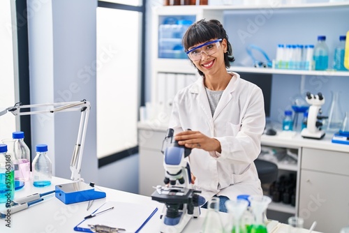 Young hispanic woman working at scientist laboratory looking positive and happy standing and smiling with a confident smile showing teeth