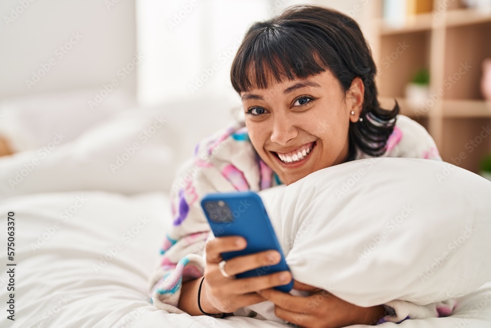 Young beautiful hispanic woman using smartphone lying on bed at bedroom Young beautiful hispanic woman using smartphone lying on bed at bedroom