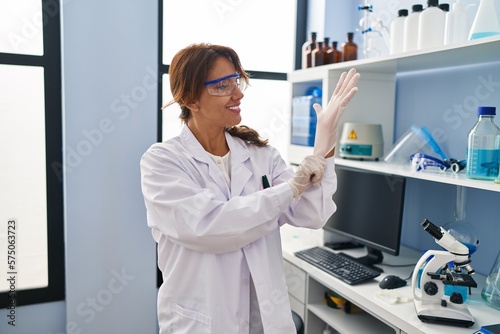 Young latin woman wearing scientist uniform and gloves at laboratory