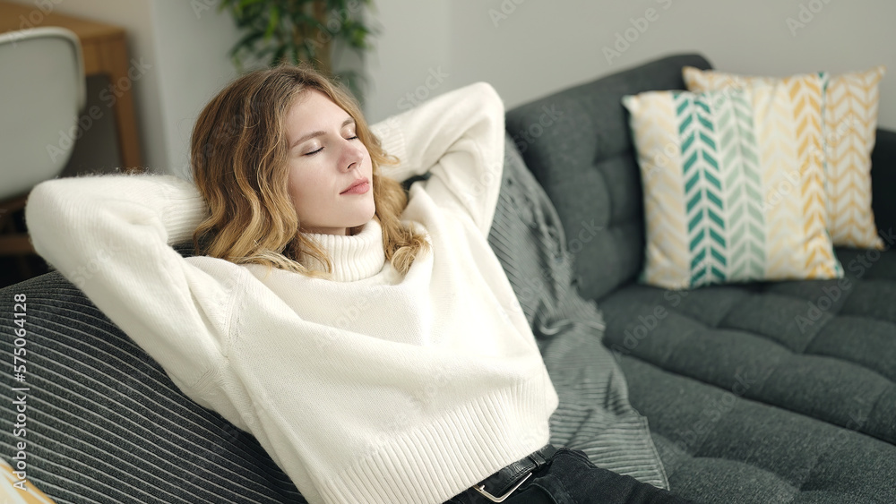 Young blonde woman relaxed with hands on head sitting on sofa at home Young blonde woman relaxed with hands on head sitting on sofa at home