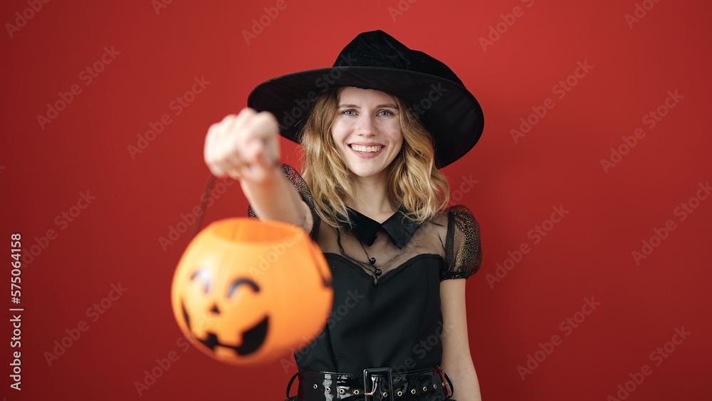 Young blonde woman wearing witch costume holding halloween pumpkin basket over isolated red background Young blonde woman wearing witch costume holding halloween pumpkin basket over isolated red background