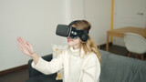 Young blonde woman playing video game using virtual reality glasses at home