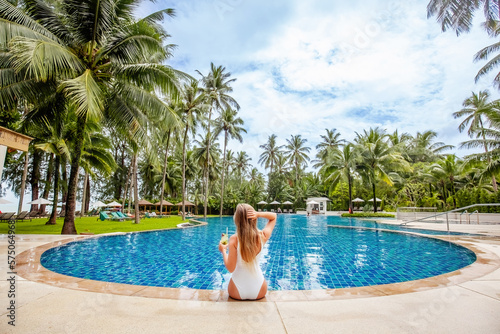 Back view of travel woman influencer with tropical cocktail sitting in swimming pool