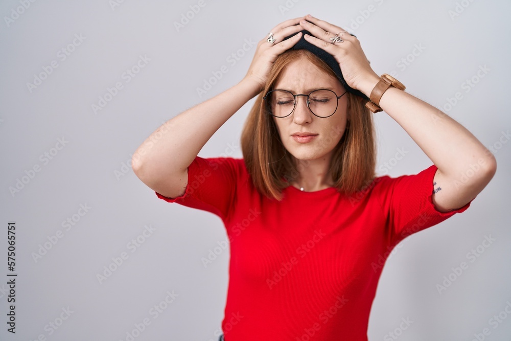 Young redhead woman standing wearing glasses and beret suffering from headache desperate and stressed because pain and migraine. hands on head. Young redhead woman standing wearing glasses and beret suffering from headache desperate and stressed because pain and migraine. hands on head.