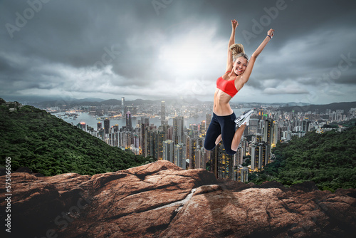 A Blond girl jumping up on rocks in front of a cityscape