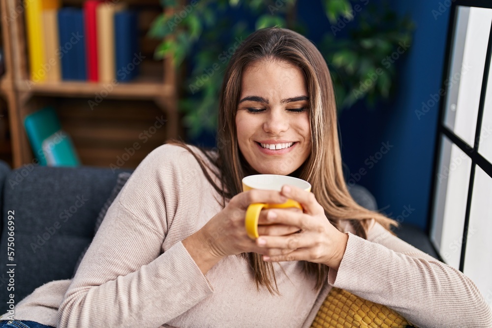 Young beautiful hispanic woman drinking coffee sitting on sofa at home Young beautiful hispanic woman drinking coffee sitting on sofa at home